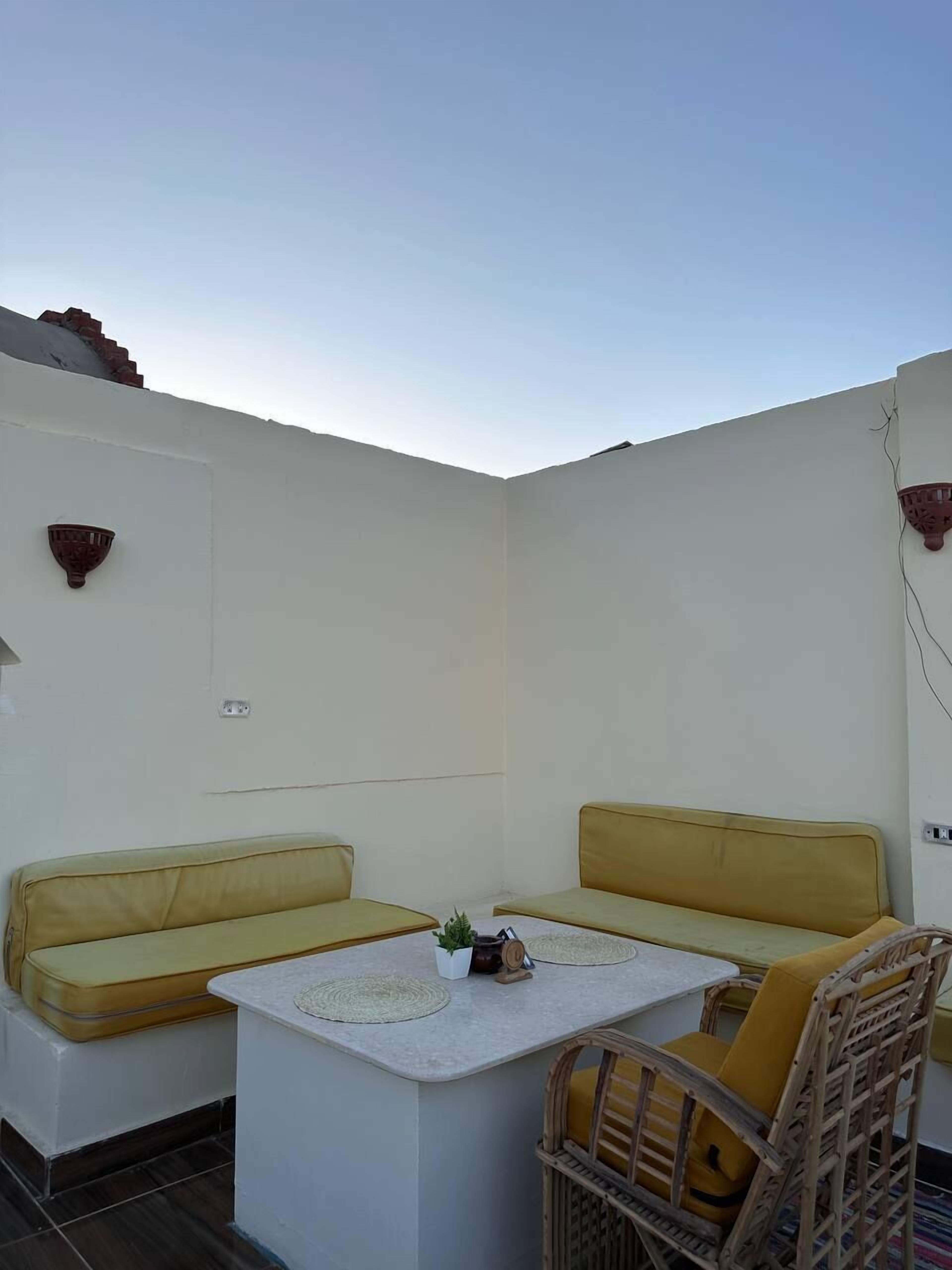 A small outdoor seating area with two yellow sofas and a table, surrounded by white walls and a clear sky.