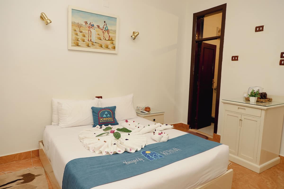 A neatly made bed with a blue towel, a pillow with a blue design, and a painting on the wall.