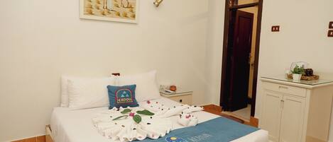 A neatly made bed with a blue towel, a pillow with a blue design, and a painting on the wall.