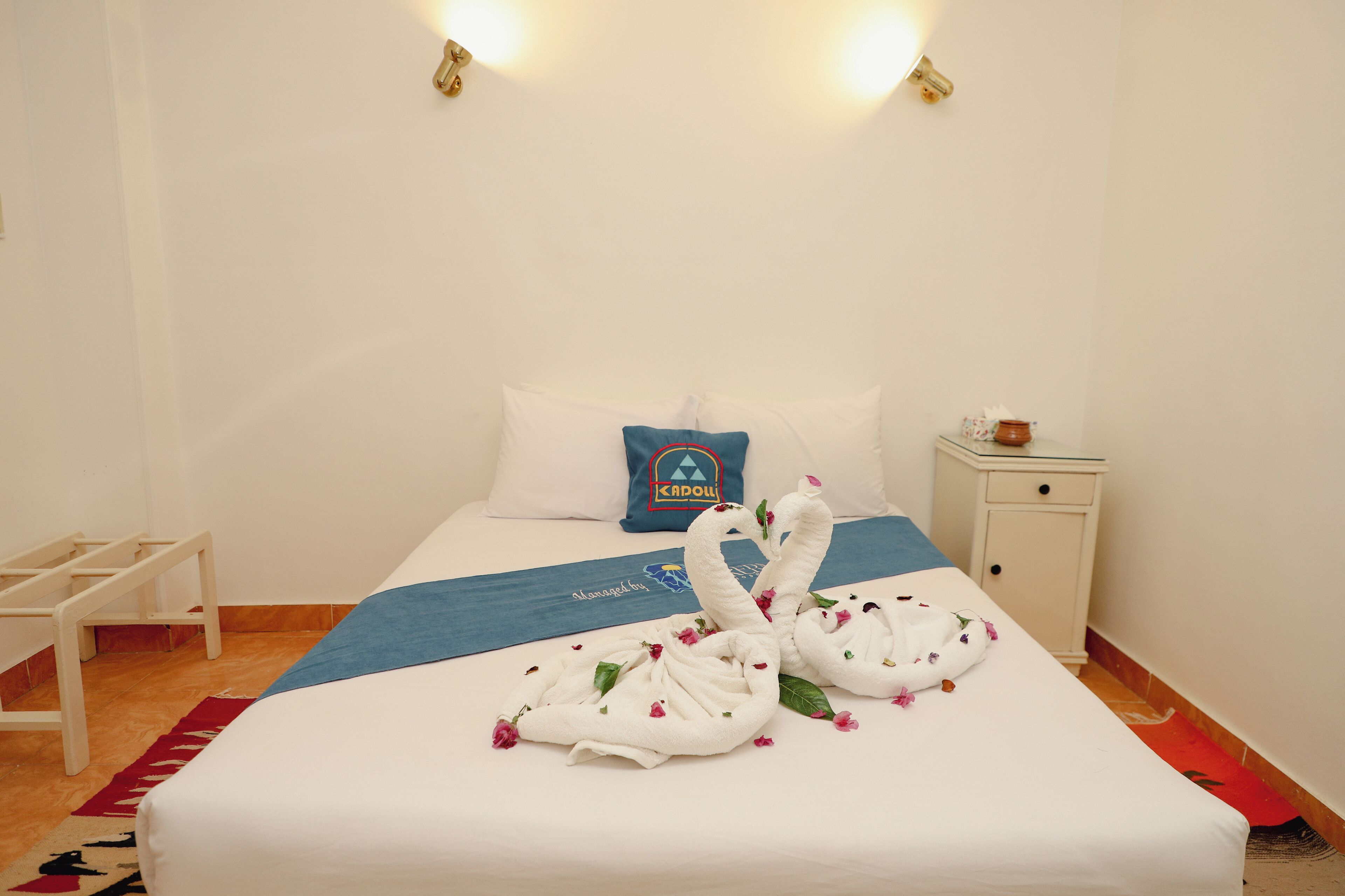 Habitación de hotel con una cama bien hecha, una toalla azul y dos toallas con forma de cisne adornadas con flores.