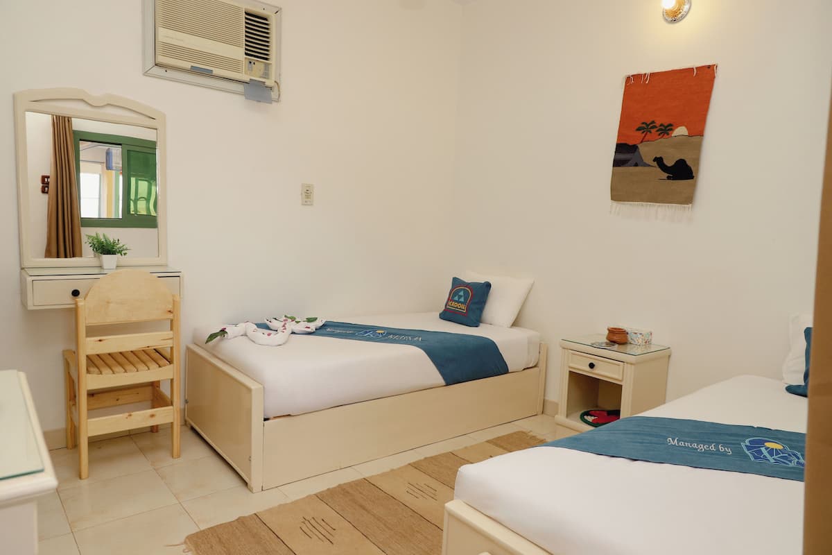 A bedroom with two beds, a wooden chair, a nightstand, a mirror, and a wall-mounted air conditioner.