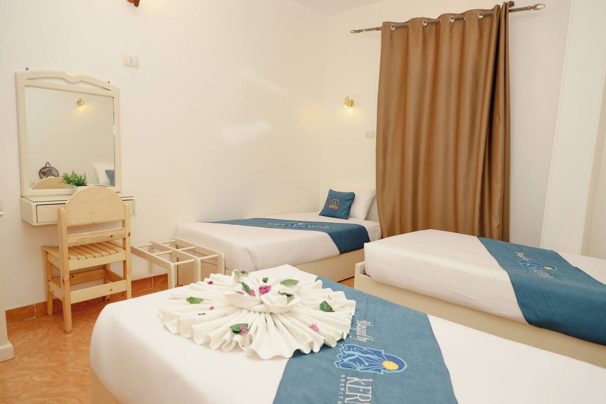 A hotel room with two beds, a wooden chair, a small table, and a mirror.
