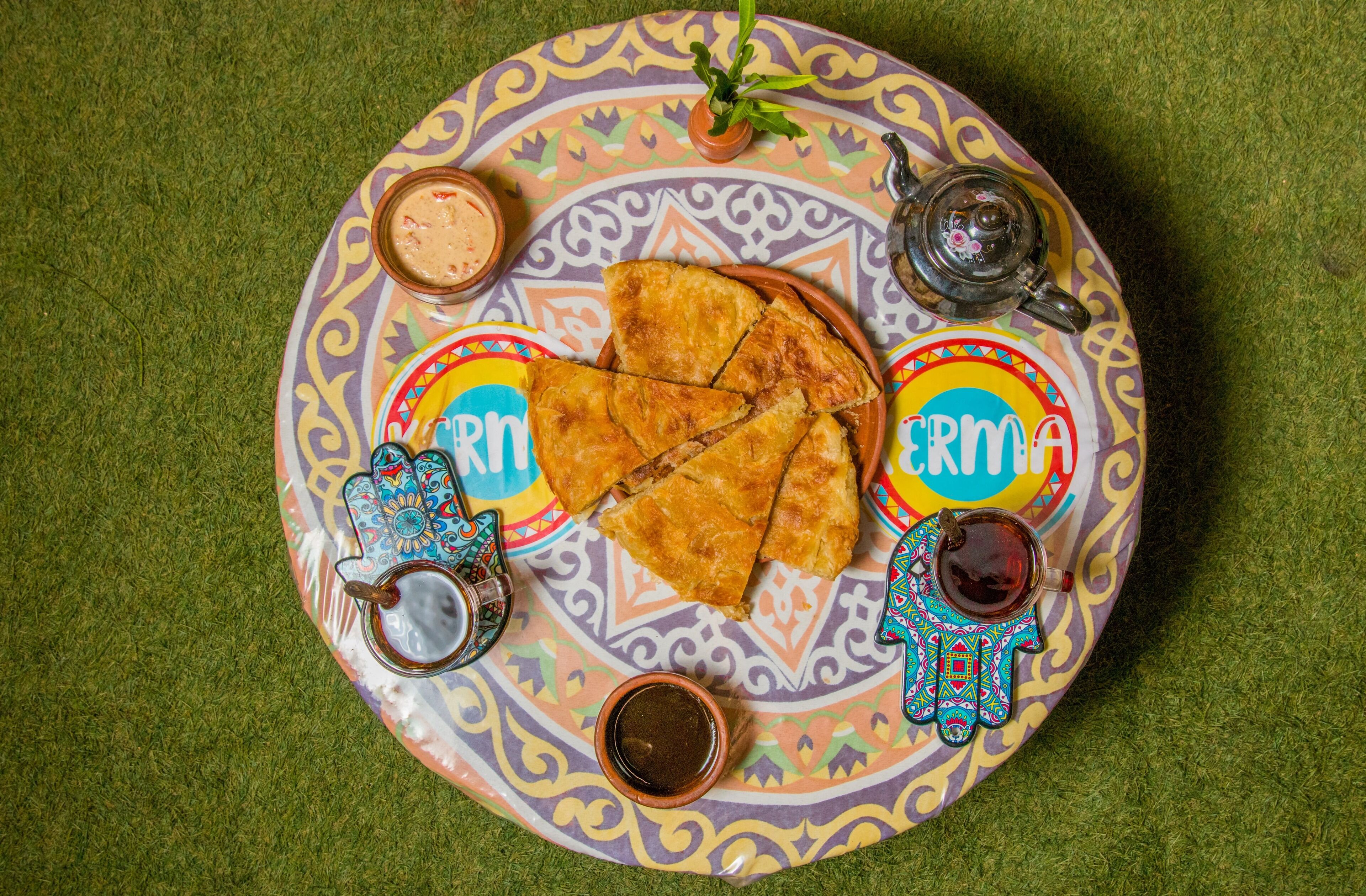 A colorful plate with food and drinks, including a pastry, a drink, and a small bowl of sauce.