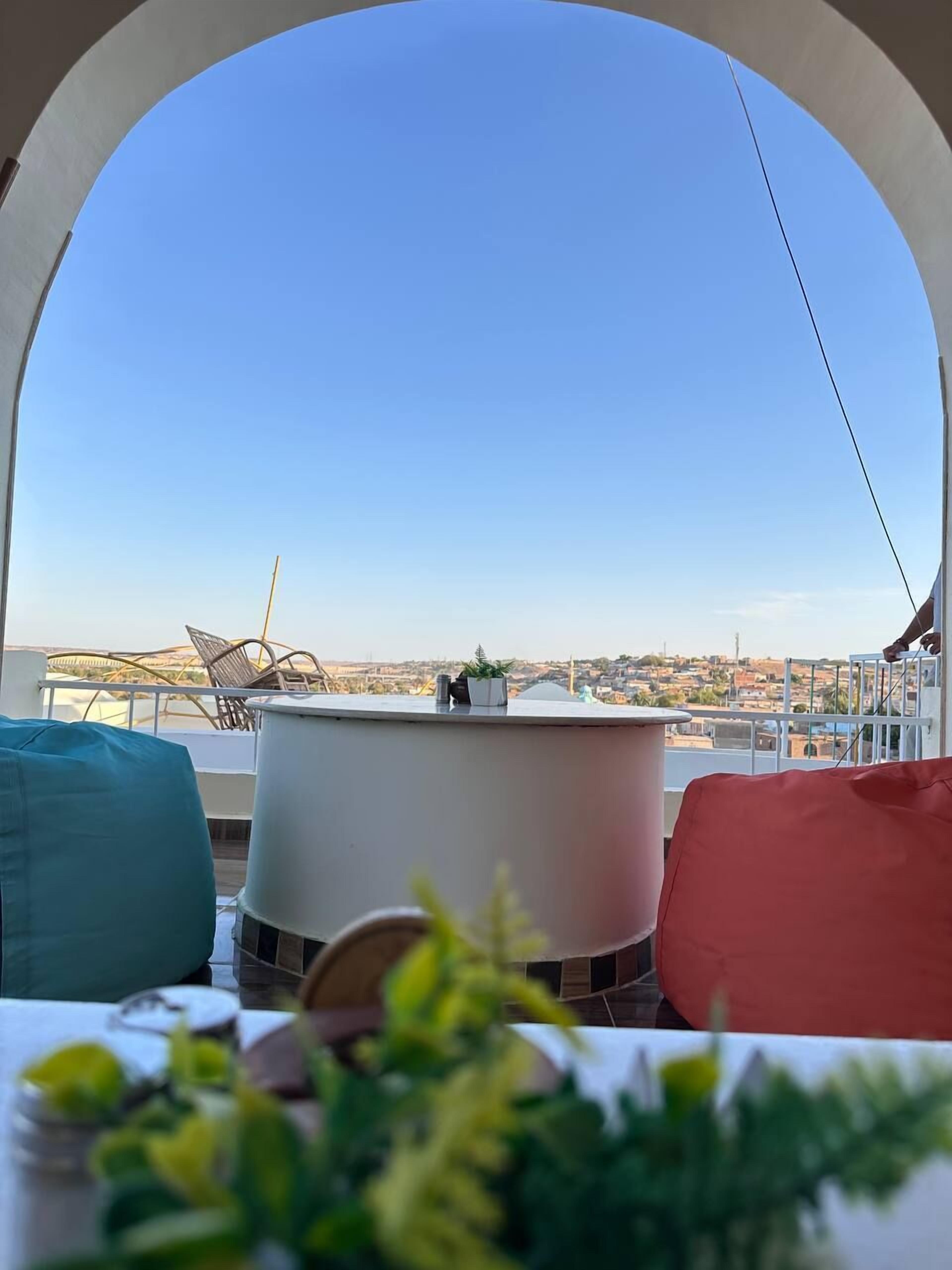 Eine Dachterrasse mit freiem Blick auf die Stadtlandschaft, einem runden Tisch und bunten Sitzgelegenheiten.