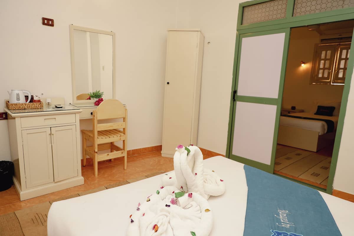 A hotel room with a bed, a desk with a kettle, a wardrobe, and a mirror.