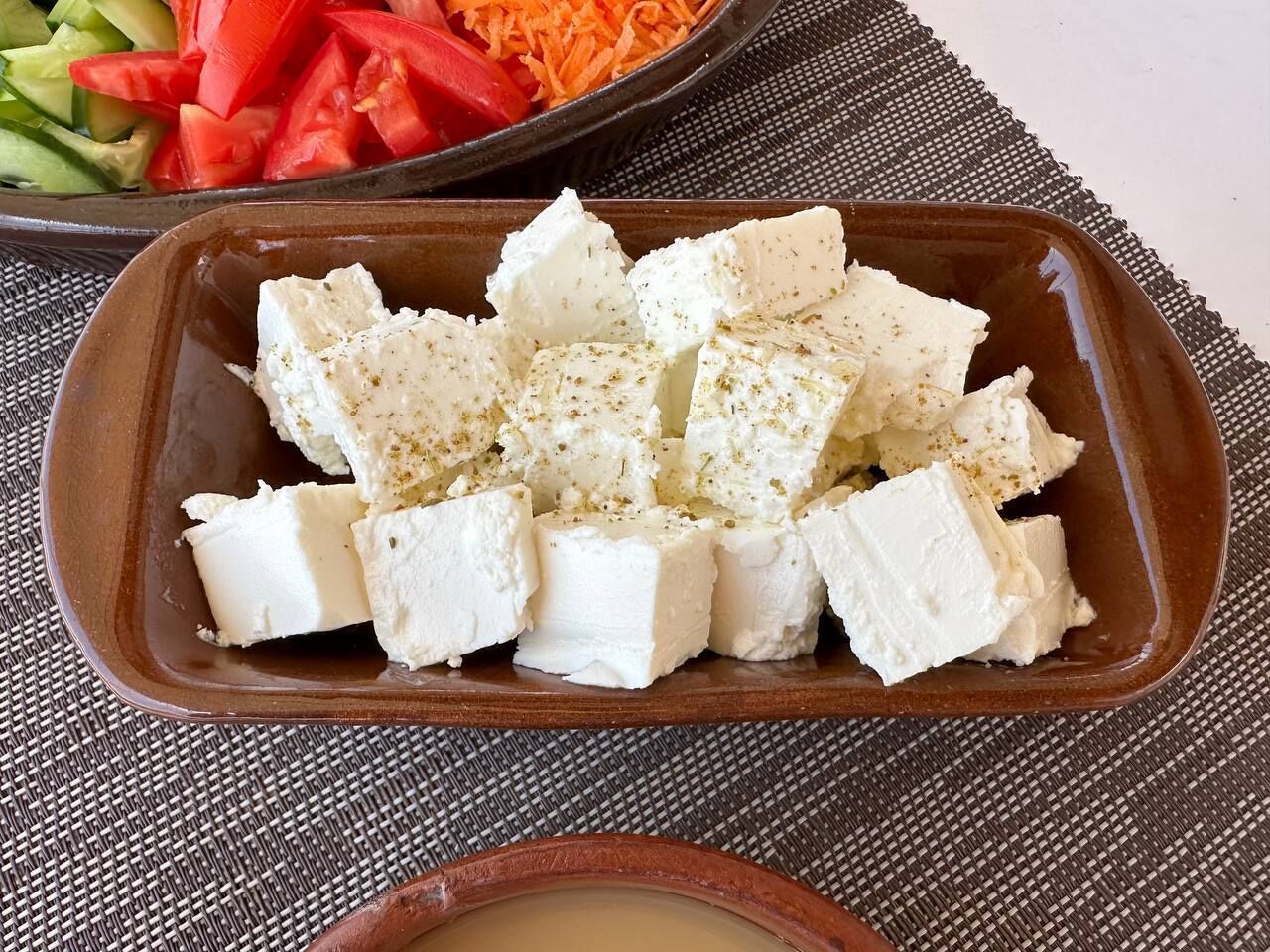 A dish of cubed white cheese, possibly feta, seasoned with herbs, served on a brown ceramic dish.