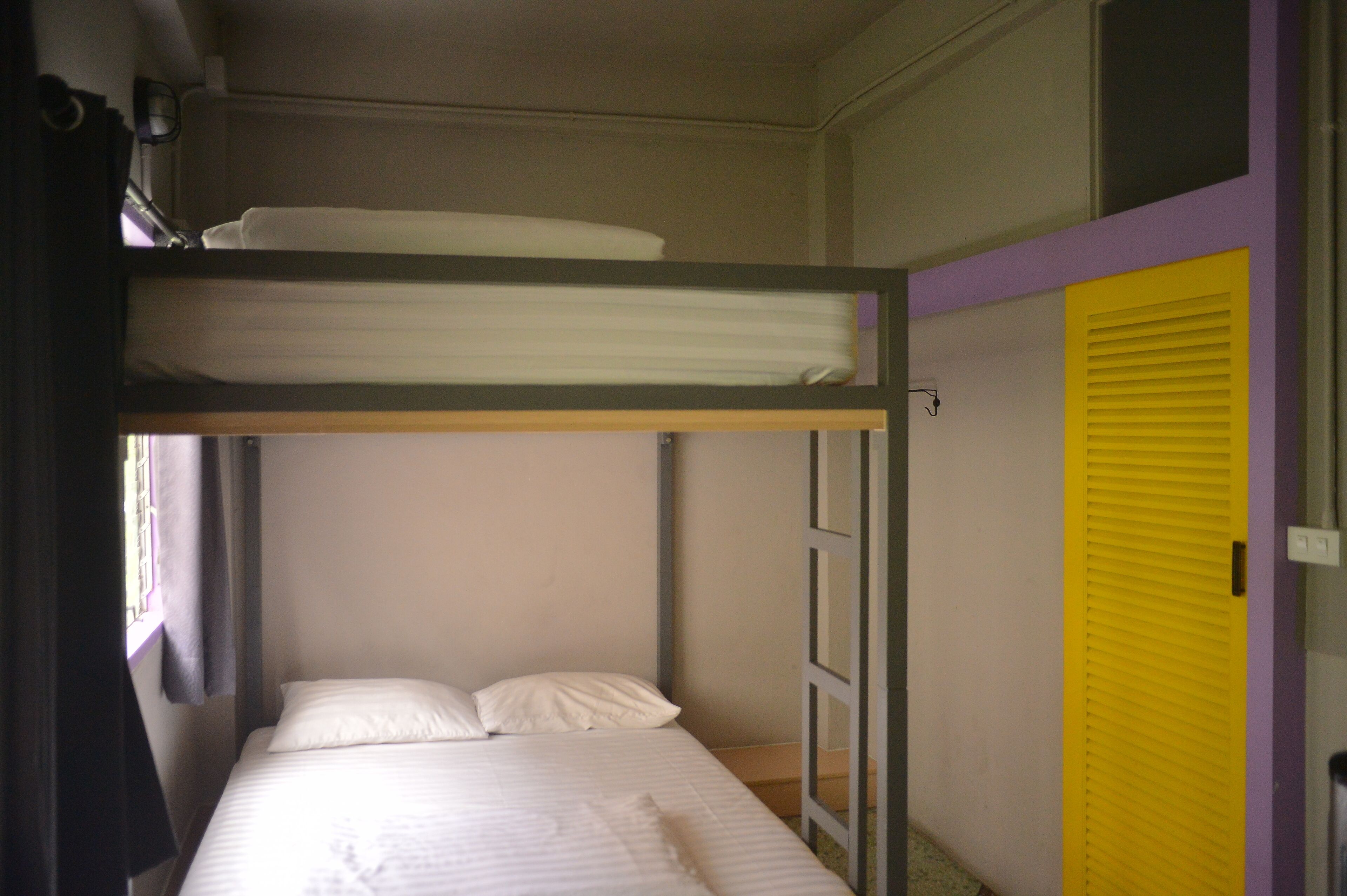 A bunk bed room with a window, a yellow door, and a white wall.