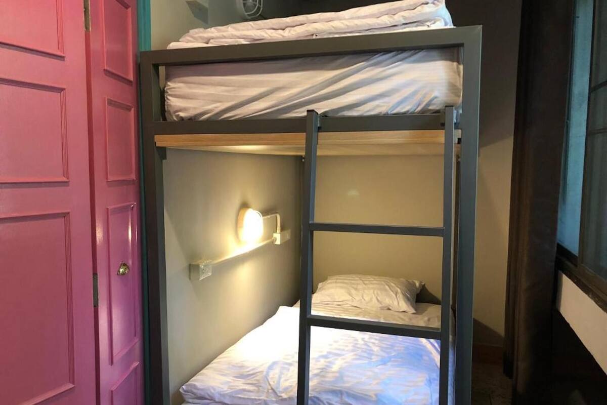 A bunk bed room with a pink door, a wall-mounted light, and a window.