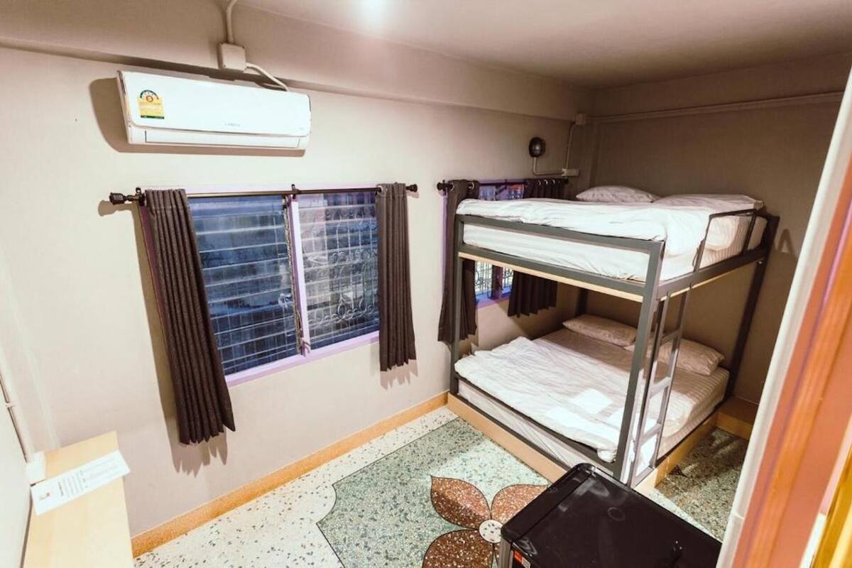 A compact room with bunk beds, a window with curtains, a ceiling fan, and a small air conditioning unit.