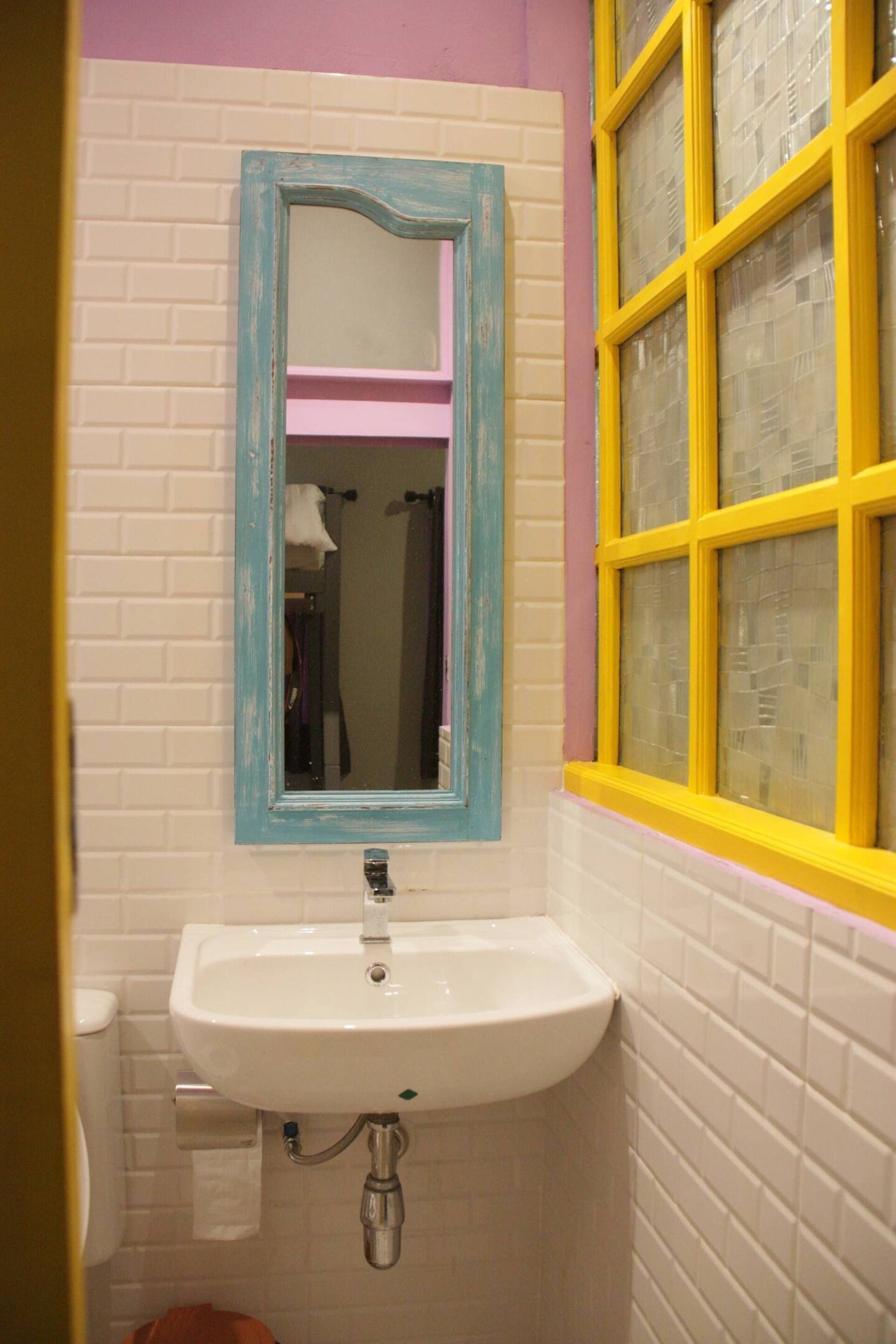 A bathroom with a white sink, a blue-framed mirror, and a yellow window.