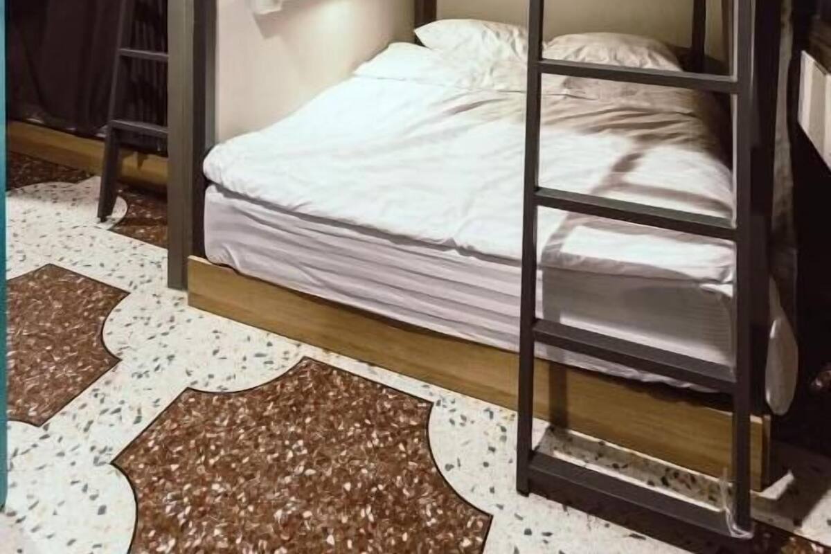 A bunk bed room with a ladder, a small shelf, and a patterned floor.