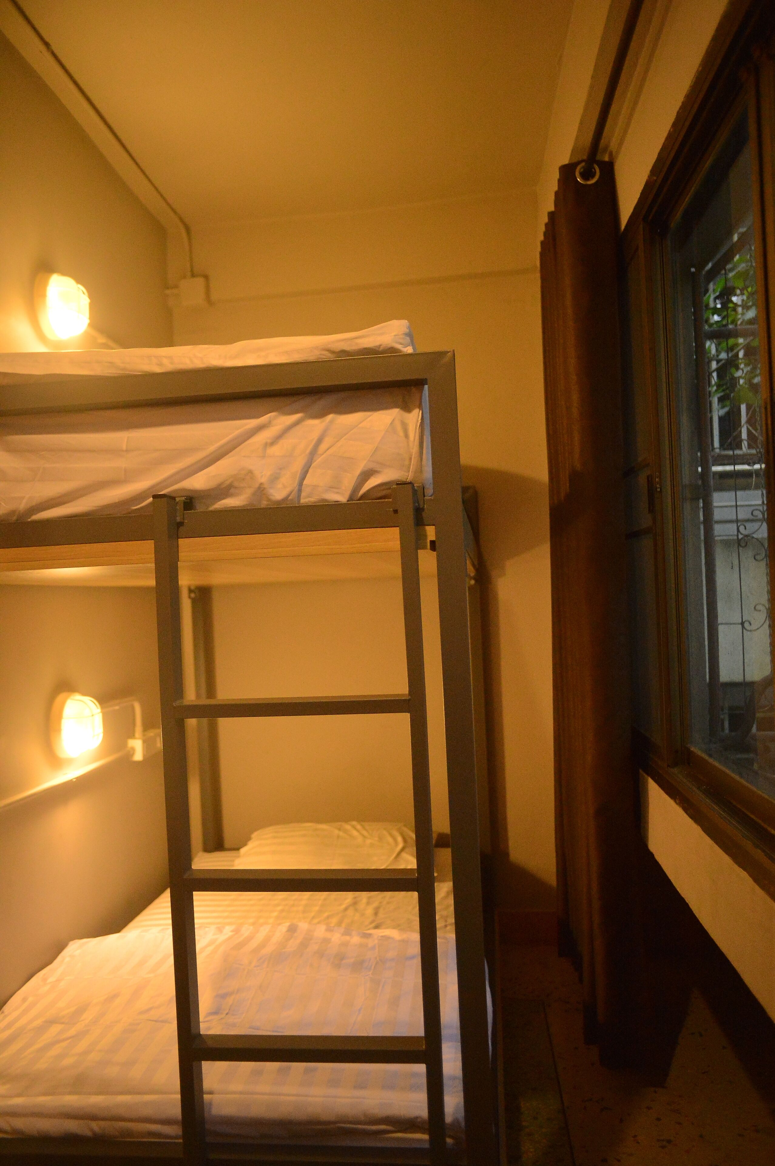A bunk bed with a ladder, a bedside lamp, and a window with curtains.