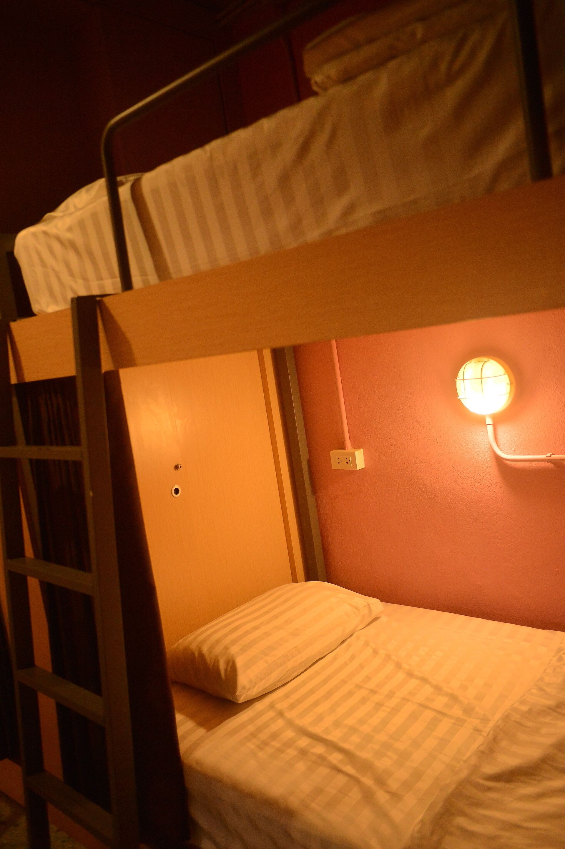 A bunk bed with a ladder, a wall socket, and a wall-mounted light fixture.