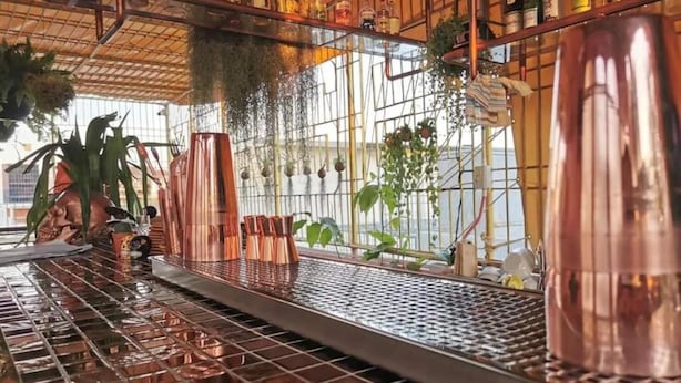 A bar area with copper mugs, a grid floor, and hanging plants. - Stash Hostel (Bangkok)