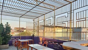 A rooftop terrace with a metal grid structure, outdoor seating, and a view of the cityscape. - Stash Hostel (Bangkok)