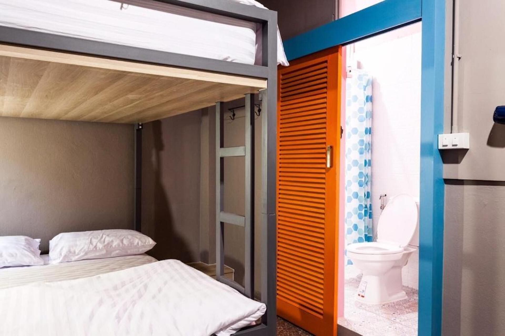A compact room with a bunk bed, a single bed, and a bathroom with a toilet and shower.