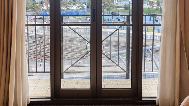 A room with a large glass door leading to an outdoor area with a view of a stadium and surrounding buildings. - Jolimont Views - Centrally located top floor apt overlooking MCG/Rod Laver (East Melbourne)