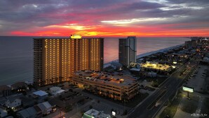 A high-rise hotel with multiple floors and a parking garage, overlooking a coastal area with a sunset view. - Pet Friendly Treasure Island 1504- Heated Pool, Gym, FREE Golf &Beach Service (Panama City Beach)