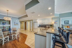 A spacious kitchen with a central island, white cabinets, and a dining area with wooden chairs. - Pet Friendly Treasure Island 1504- Heated Pool, Gym, FREE Golf &Beach Service (Panama City Beach)