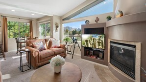 Ein geräumiges Wohnzimmer mit Kamin, Fernseher und einem großen Fenster mit Blick auf die Berge.