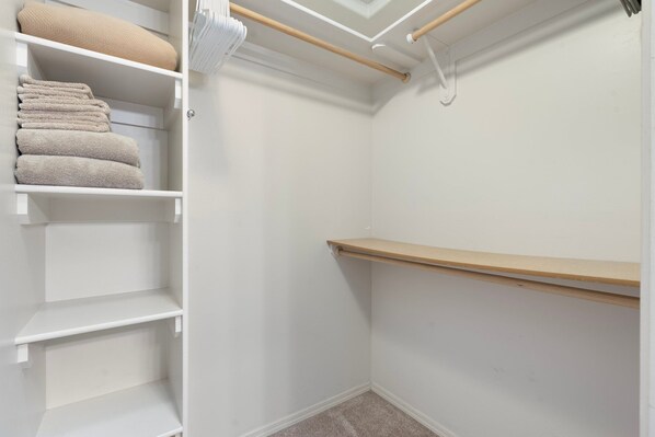 Un vestidor con estantes blancos y un estante de madera.