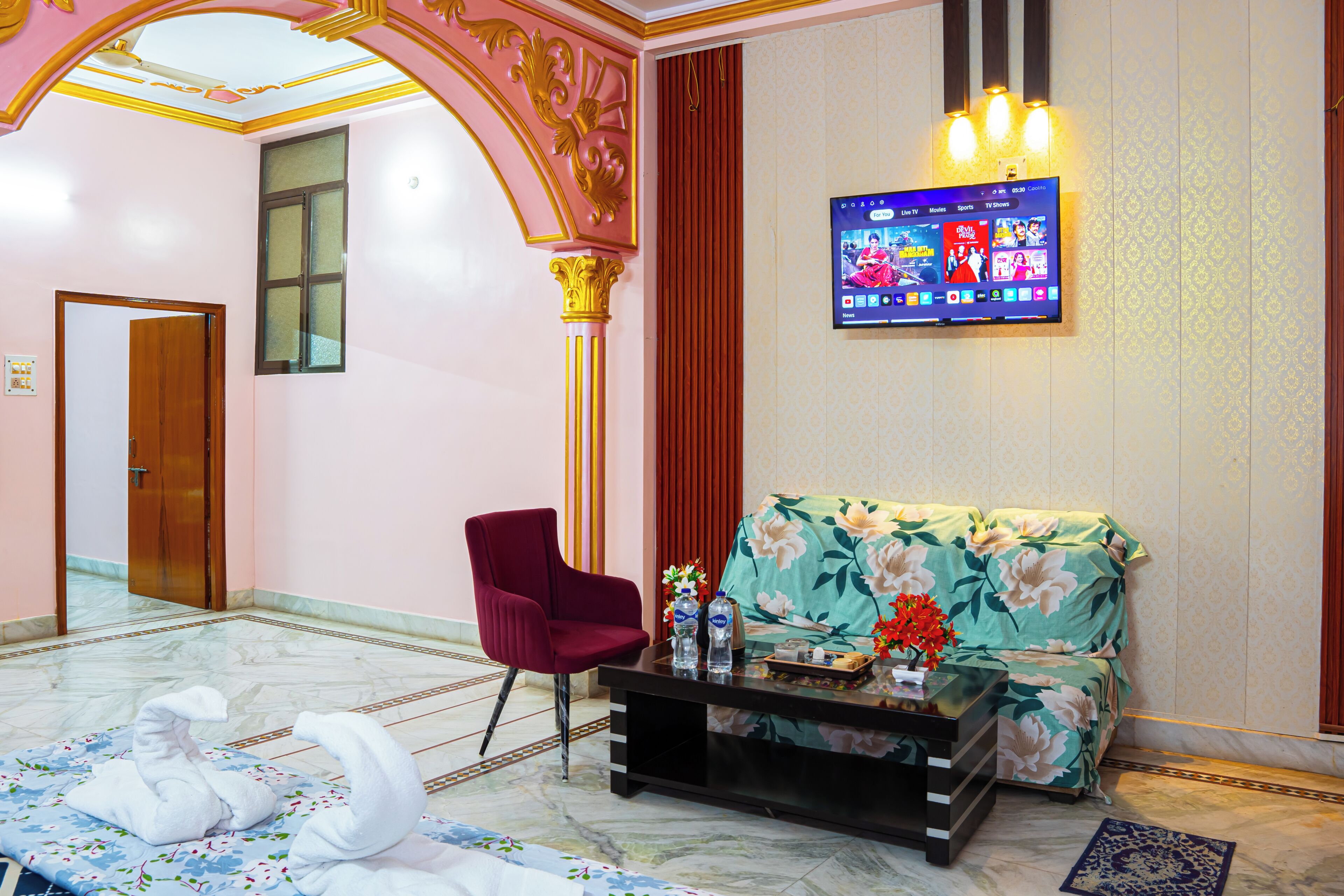A hotel lobby with a reception desk, a sofa, a chair, and a TV mounted on the wall.