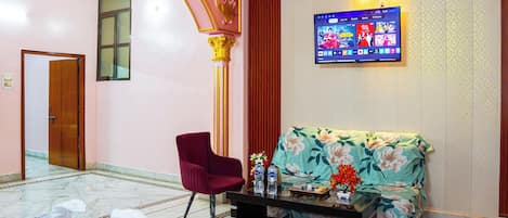 Un hall de hotel con mostrador de recepción, un sofá, una silla y un televisor montado en la pared.