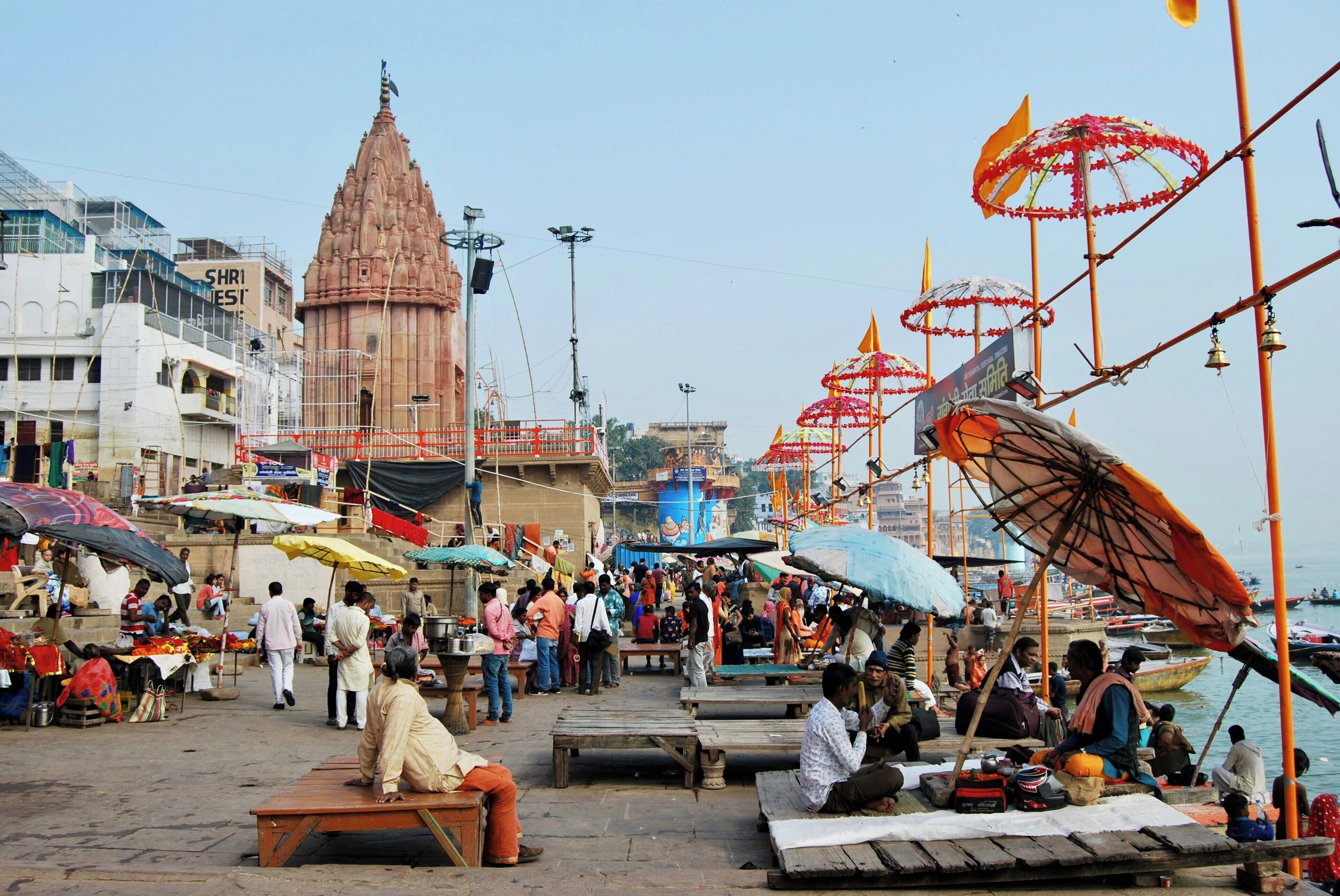 A crowded riverside area with people, boats, and a prominent temple structure.