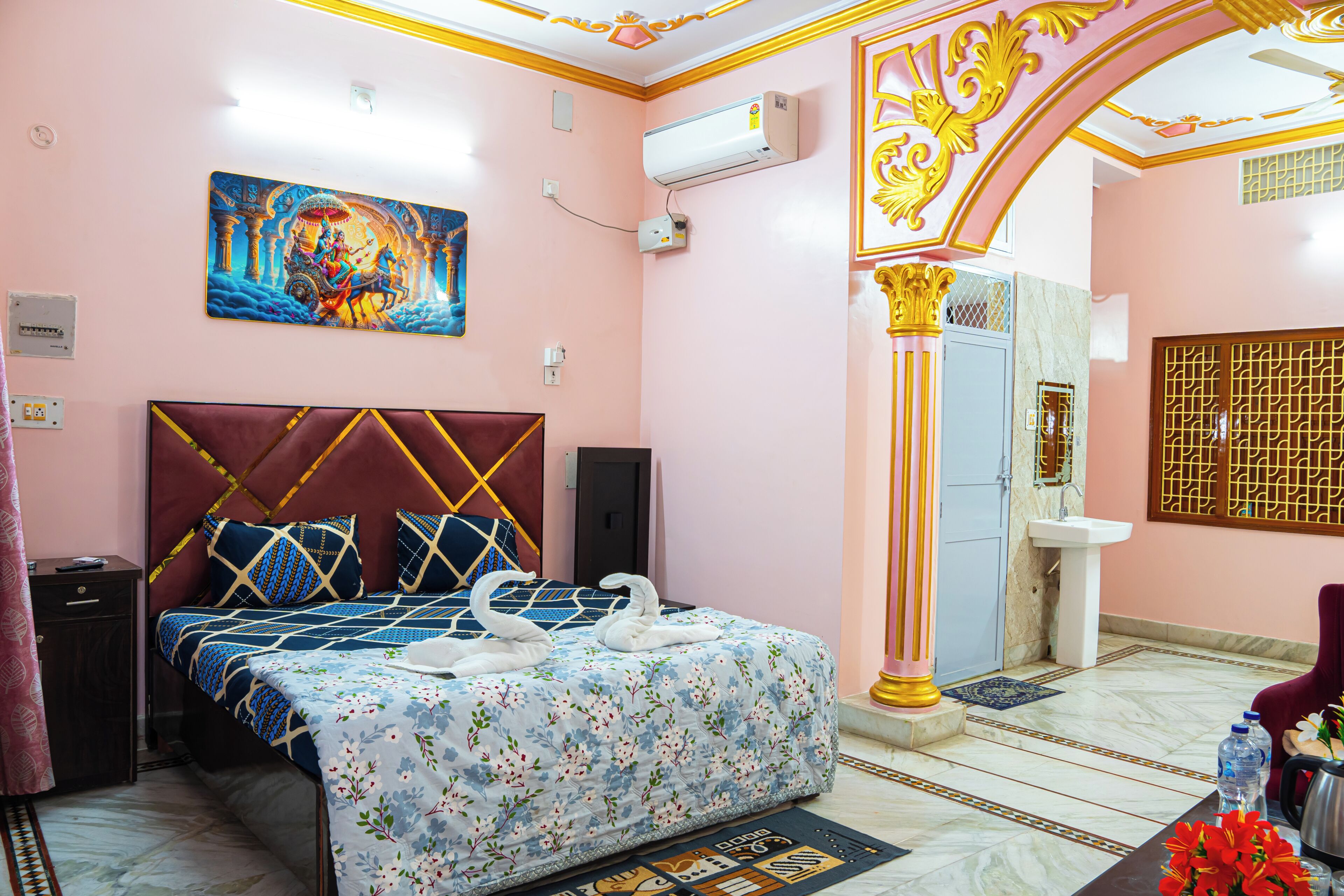 A hotel room with a bed, a painting, an air conditioning unit, and a bathroom visible through an open door.