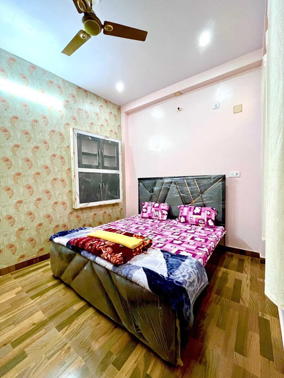 A bedroom with a bed, a ceiling fan, a window, and patterned wallpaper.