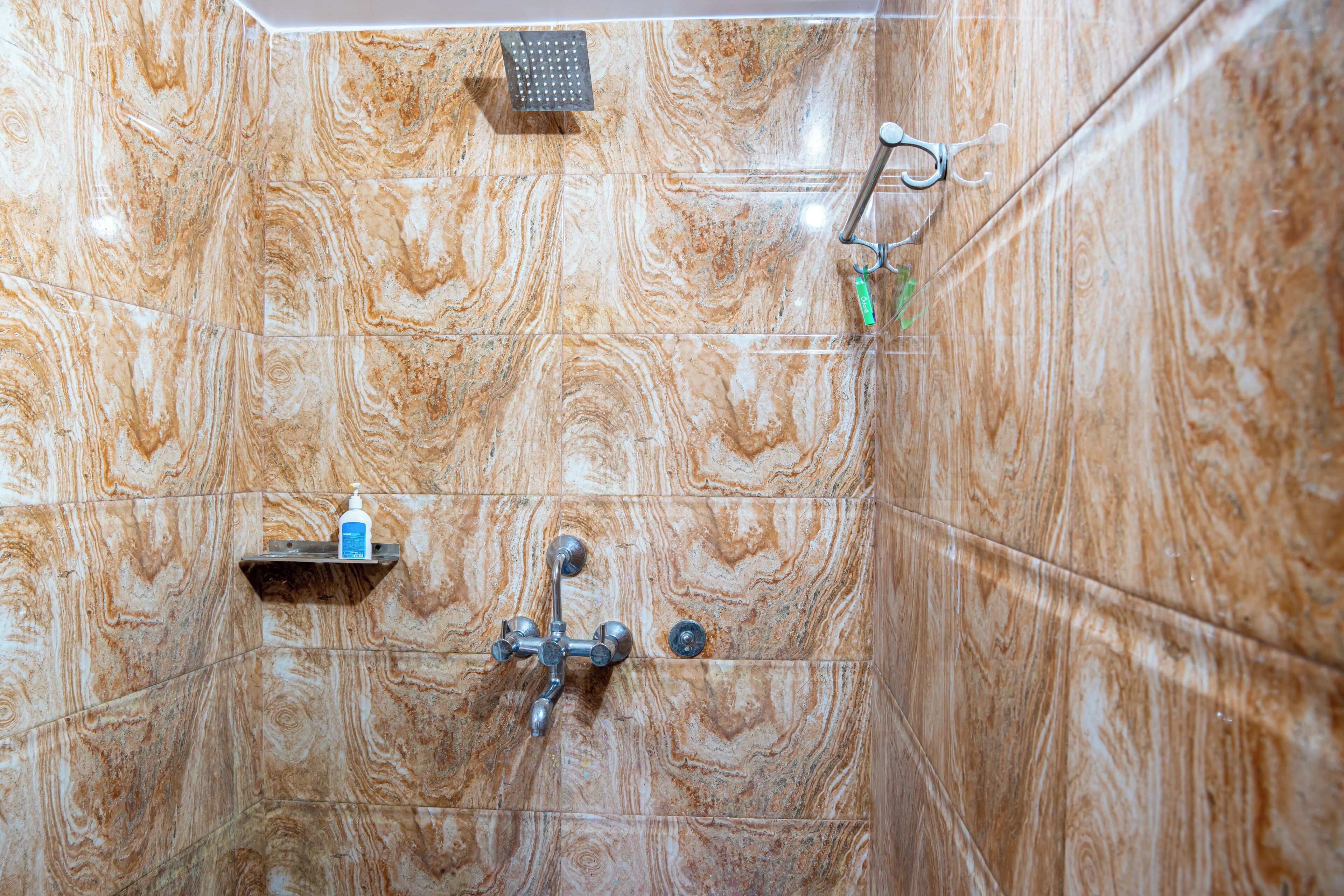 A bathroom with a marble wall, a handheld showerhead, a handheld shower attachment, and a bottle of shampoo.
