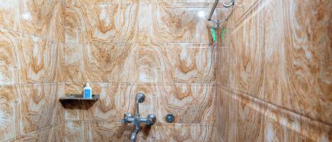 Un baño con pared de mármol, cabezal de ducha de mano y un dispensador de champú.