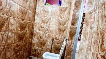 A bathroom with marble walls, a toilet, and a shower area.