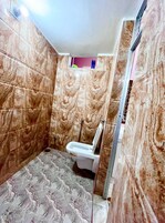A bathroom with marble walls, a toilet, and a shower area.