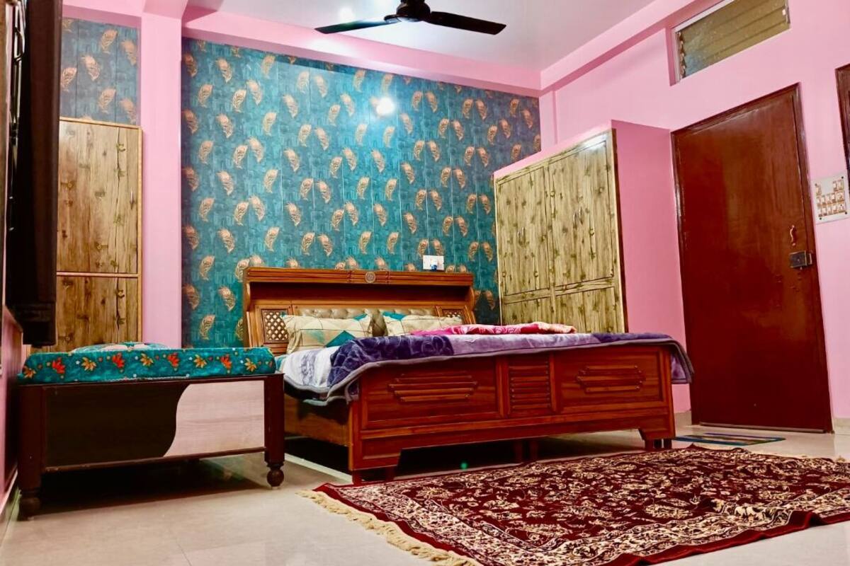 A bedroom with a bed, a wooden wardrobe, a bench, and a patterned wall.