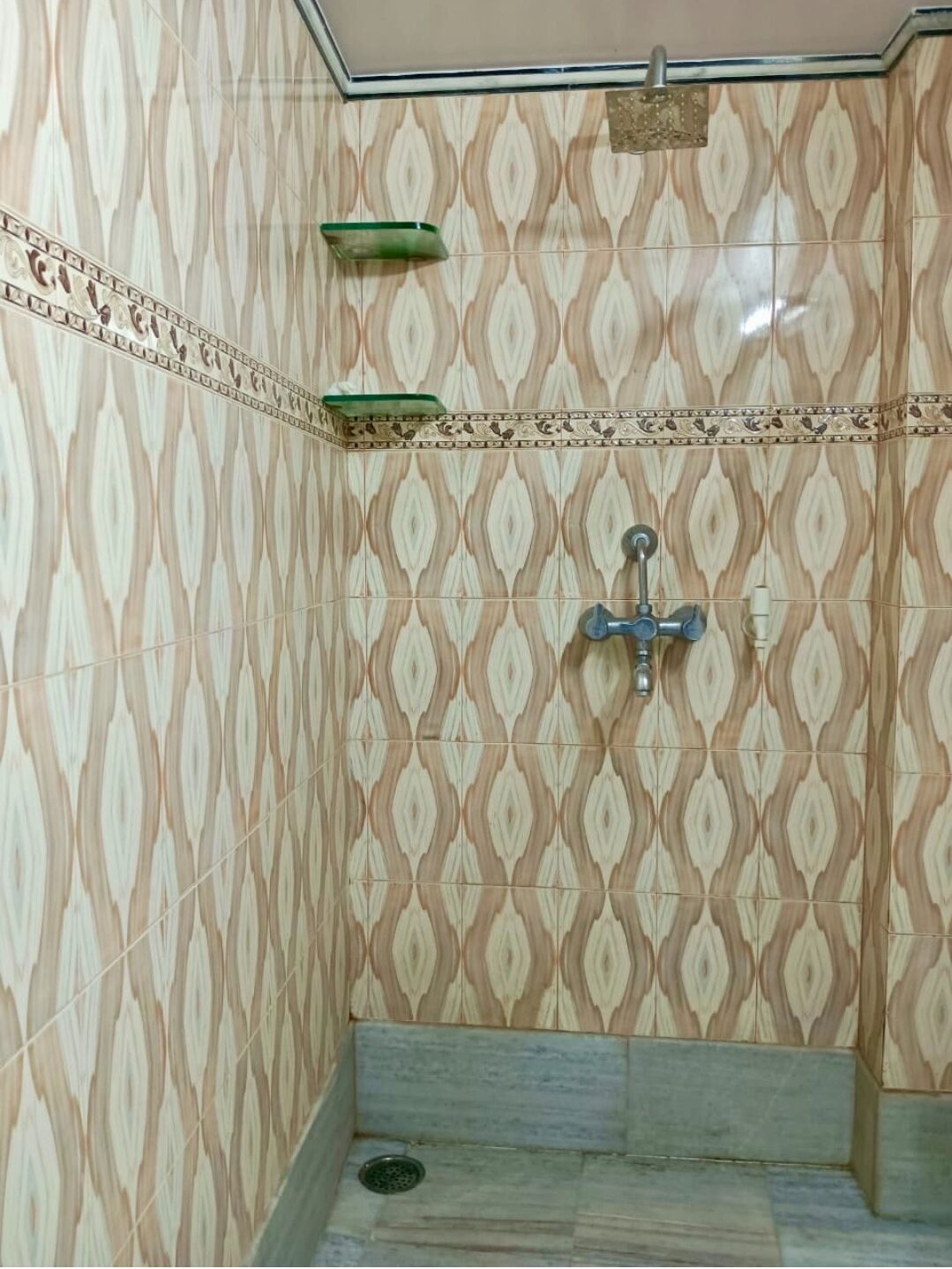 A bathroom with patterned tiles, a shower, and a green shelf.