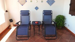 Two reclining chairs with metal frames and blue cushions, a small table with a red object, and decorative tiles on the wall.