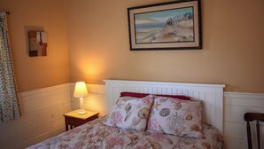 A bedroom with a bed, a nightstand with a lamp, a painting on the wall, and a window with curtains.