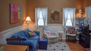 A living room with a blue sofa, a small table, a colorful chair, a television, and a mirror on the wall.
