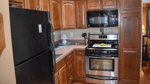 A kitchen with wooden cabinets, a black refrigerator, a microwave, and a stainless steel oven.