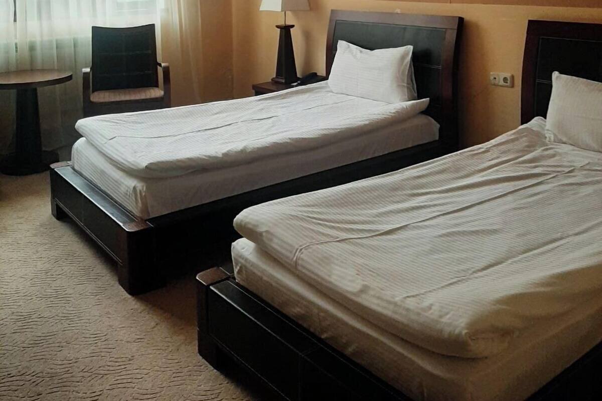 Une chambre d’hôtel avec deux lits, une chaise, une petite table et une lampe.