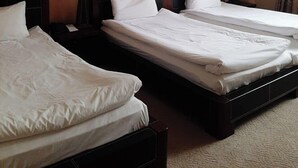 Een hotelkamer met twee bedden, elk voorzien van witte lakens, een donker hoofdeinde en een nachtkastje met een lamp.