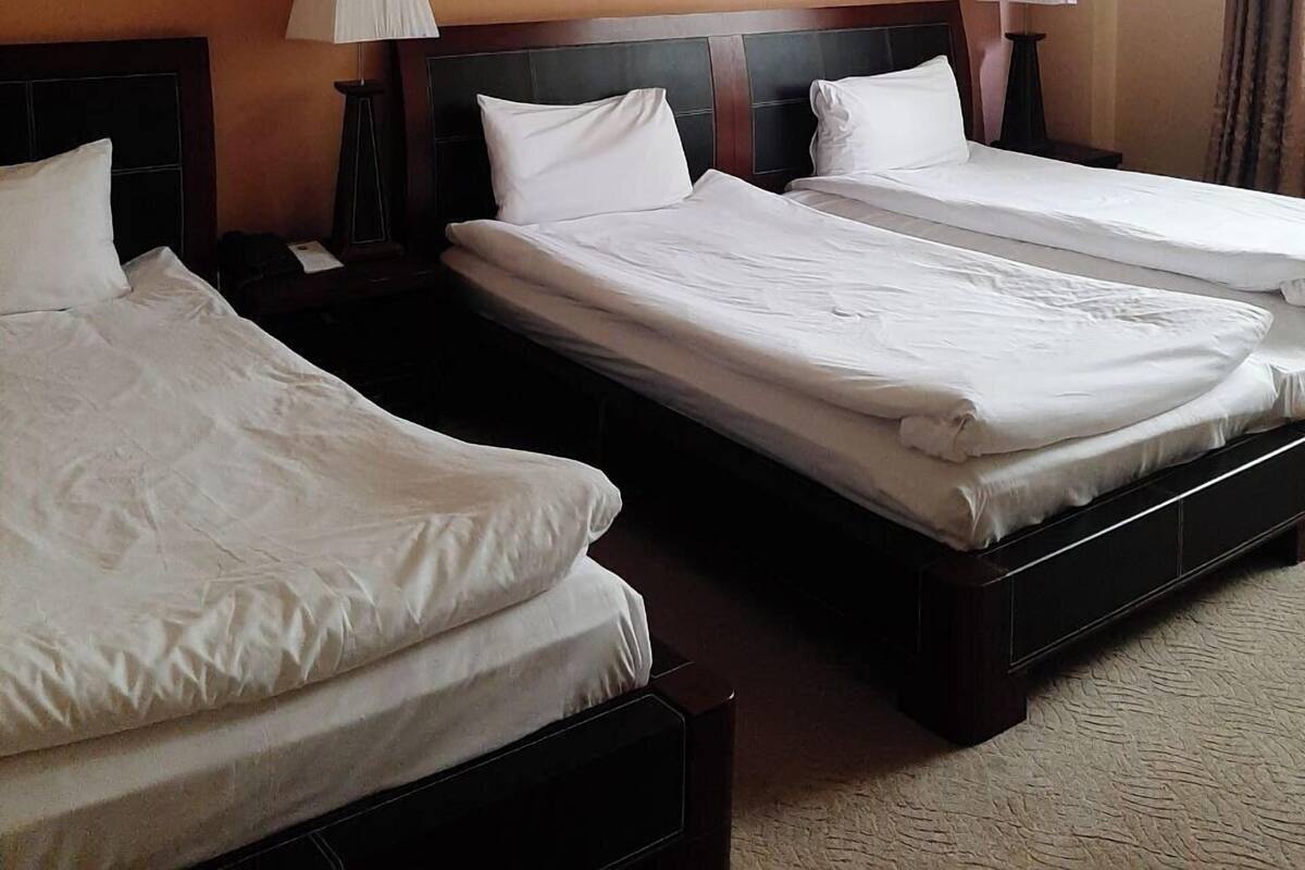 Une chambre d’hôtel avec deux lits, chacun doté de draps blancs, d’une tête de lit sombre et d’une table de chevet avec une lampe.