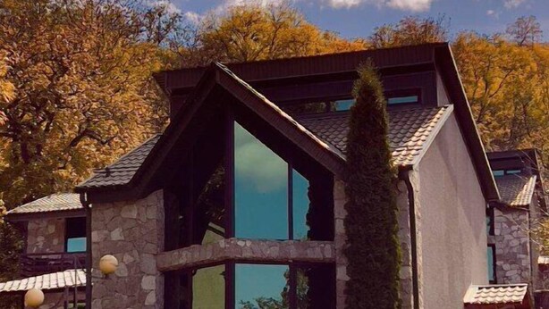Een modern huis met een gevel van natuursteen, grote glasramen en een schuin dak.