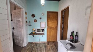 Ein schmales Entree mit einer Holztür, einer Mikrowelle auf einem Regal und einem Kühlschrank mit Flaschen darauf.
