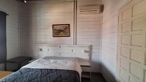 Ein Schlafzimmer mit Bett, Nachttisch, Wand-Klimaanlage und einem gerahmten Bild an der Wand.