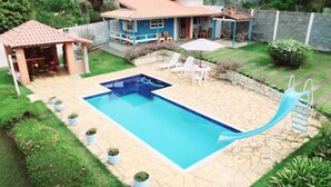 Ein rechteckiger Swimmingpool mit Rutsche, umgeben von Steinplatten und Blumentöpfen.