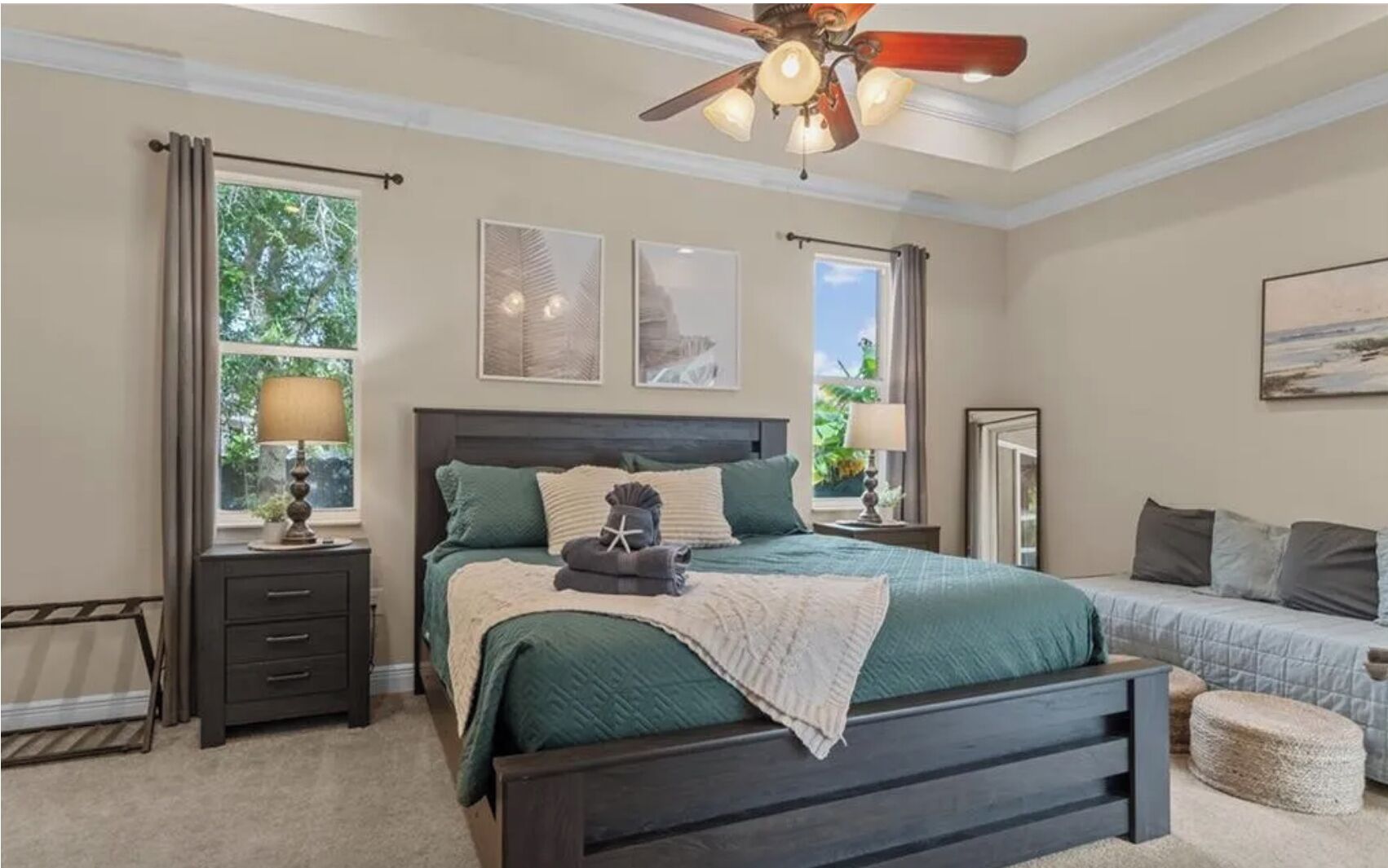 Une chambre à coucher avec un grand lit, des tables de chevet, un ventilateur de plafond et des œuvres d’art accrochées aux murs.