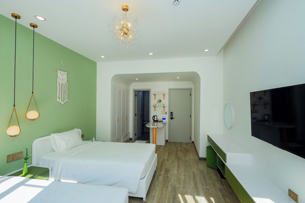 Ein Hotelzimmer mit Bett, Nachttisch und Fernseher. Ein Flur führt zu einem Badezimmer und einer Küchenzeile.