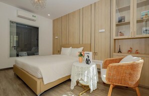 Ett hotellrum med en stor säng, ett litet bord med en vas, en stol och ett skåp med dekorativa föremål.